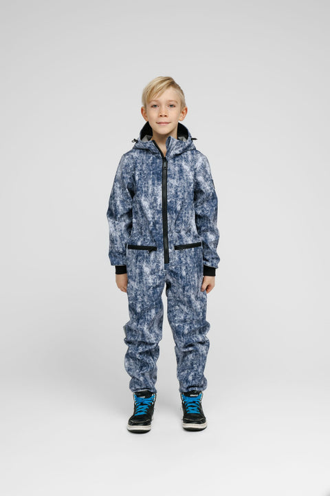 1. Child wearing blue patterned softshell onesie with hood and black sneakers standing in studio