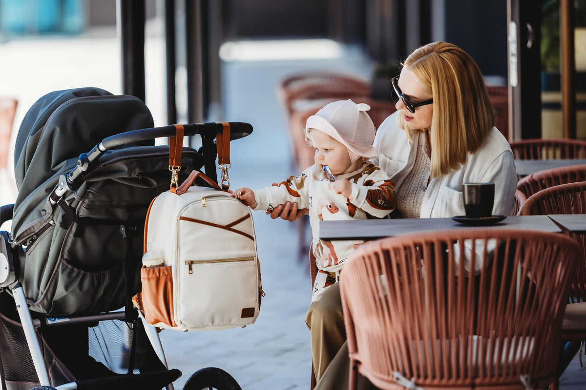 3. Woman sitting with child and Ally Scandic small cappuccino diaper backpack attached to stroller