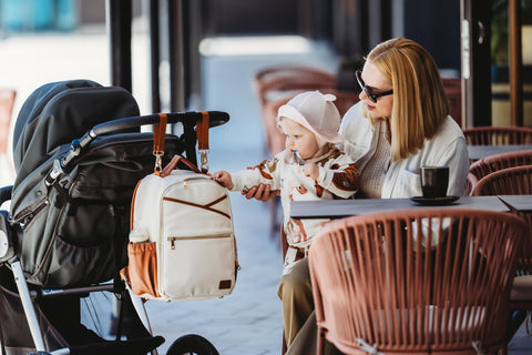 3. Woman sitting with child and Ally Scandic small cappuccino diaper backpack attached to stroller