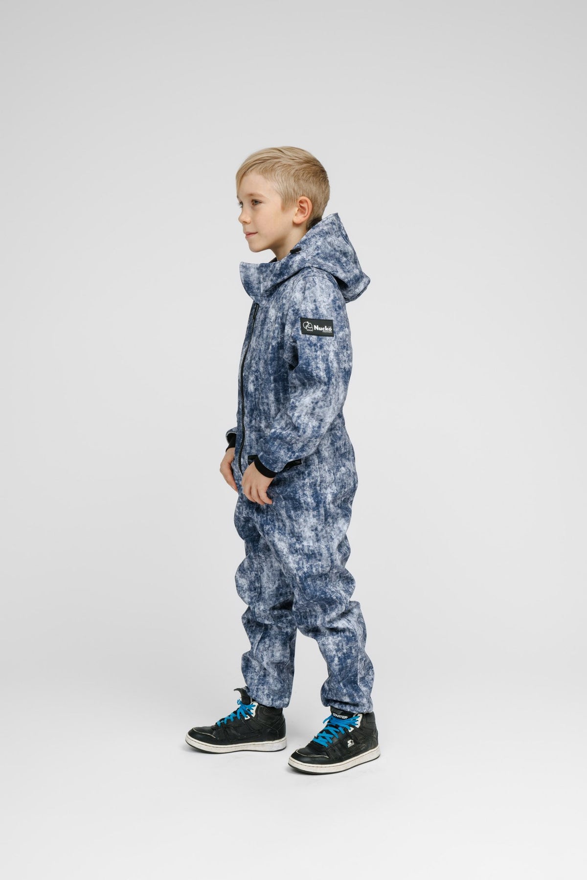 3. Side view of child in blue patterned softshell onesie with hood and black sneakers in studio