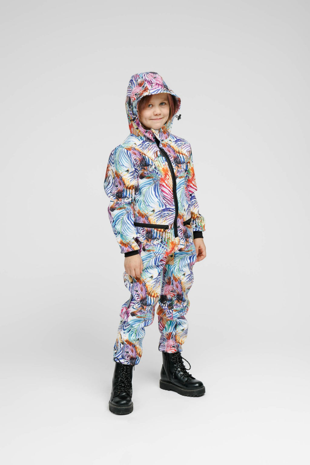 1. Child wearing Nuckö rainbow softshell onesie with hood, standing in studio setting