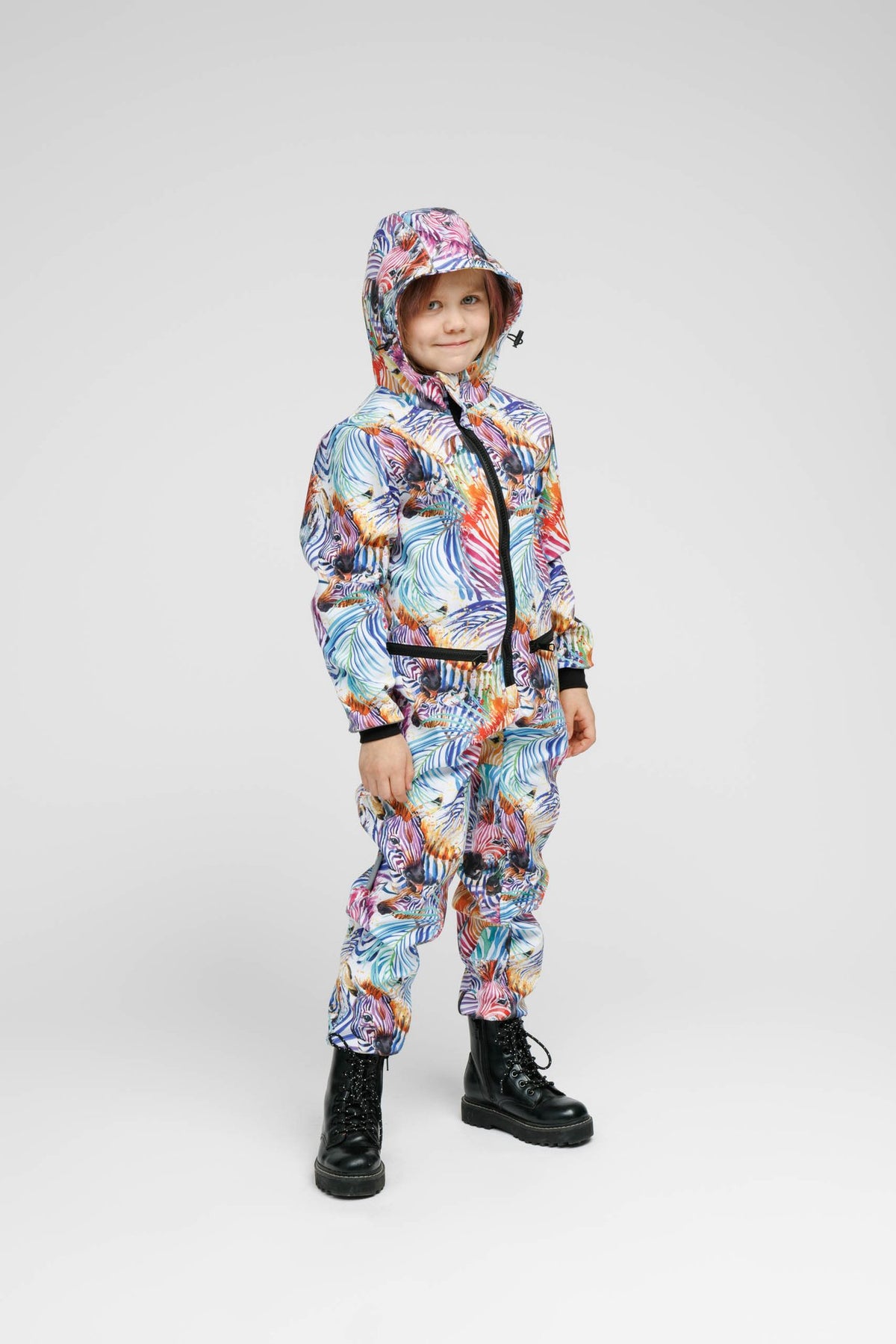 1. Child wearing Nuckö rainbow softshell onesie with hood, standing in studio setting