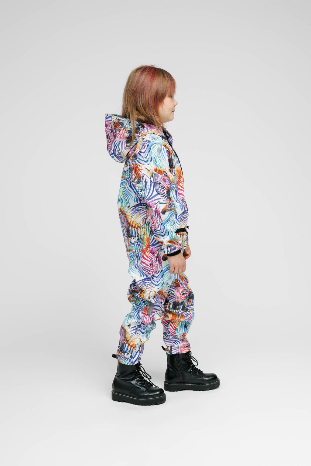 3. Side view of child in Nuckö rainbow softshell onesie with hood, studio background