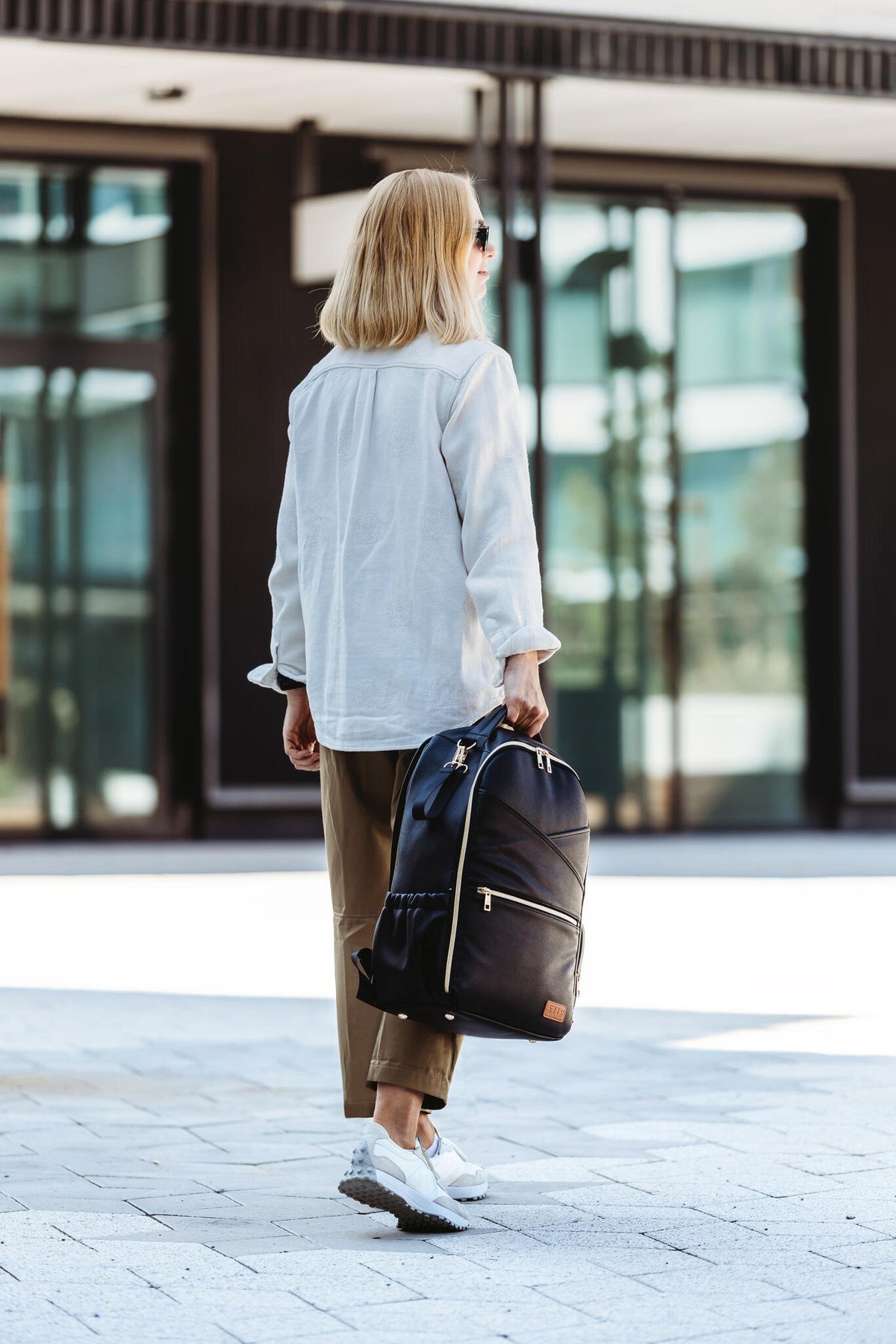 4. Woman walking with Ally Scandic Espresso Diaper Backpack, showing stylish design and functionality