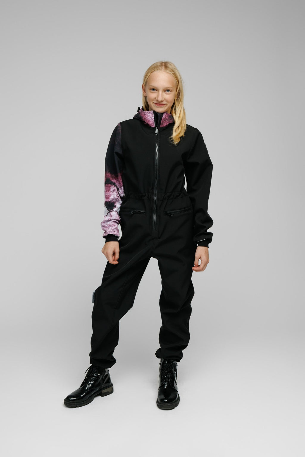 1. Girl wearing Nuckö Pilv softshell onesie in black with purple accents, front view in studio