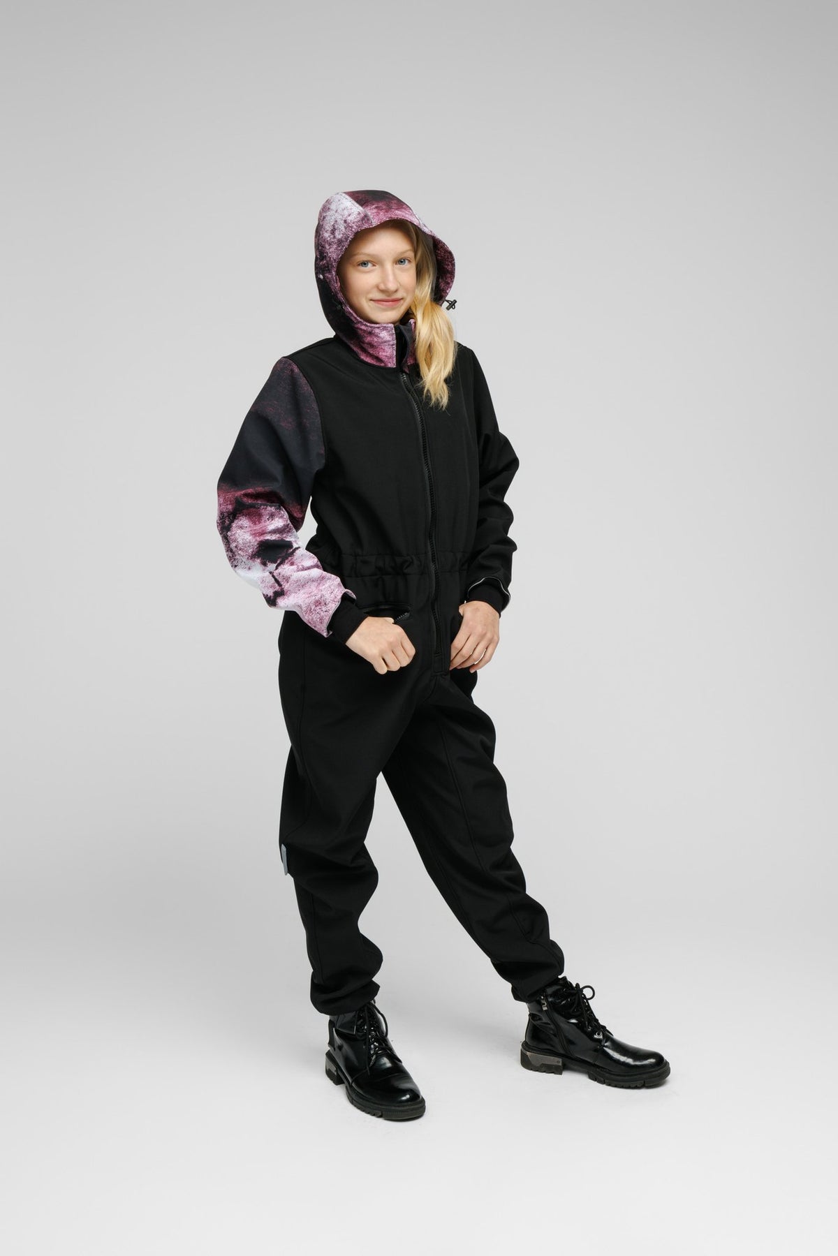 5. Girl in Nuckö Pilv softshell onesie with hood up, displaying waterproof fabric and zippered pockets
