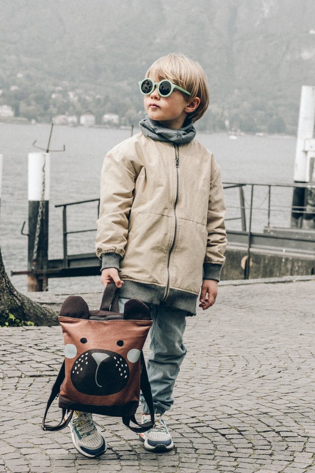 4. Child with Muni bear backpack running on cobblestone, playful outdoor scene
