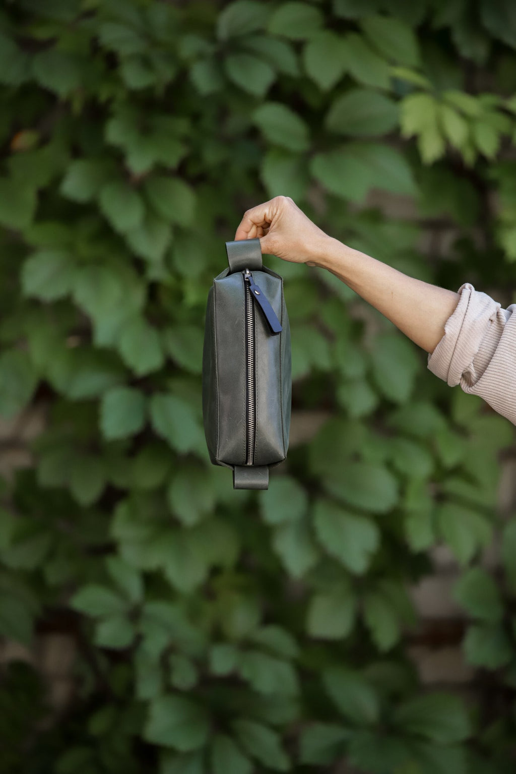 2. Side view of eleriinseim leather cosmetic bag in Forest color held by a woman