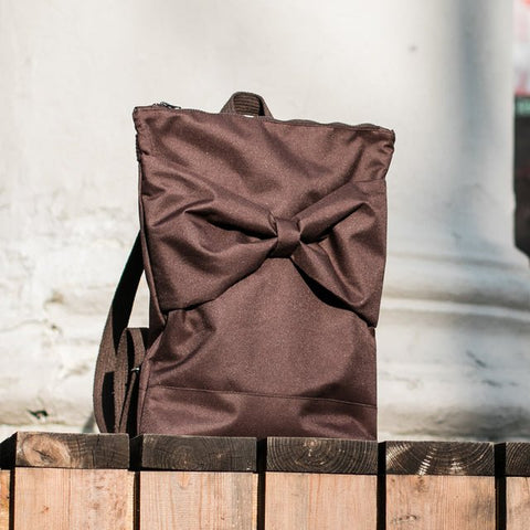 5. MUNI brown backpack with bow placed on wooden surface against white wall