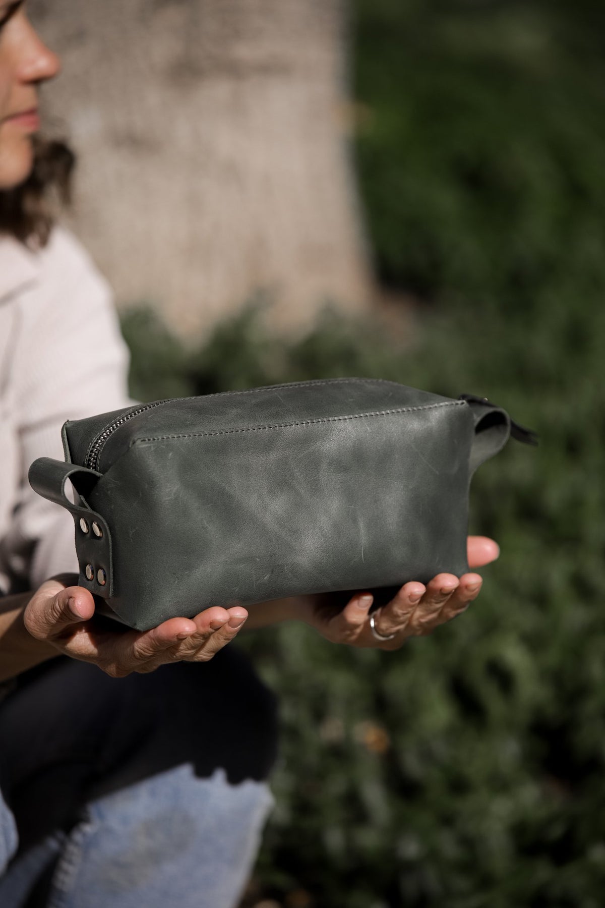 1. Woman holding eleriinseim leather cosmetic bag in Forest color outdoors