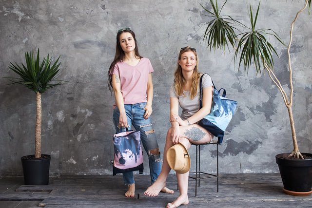 1. Two women showcasing Muni Watercolor backpacks in pink and blue in a lifestyle setting