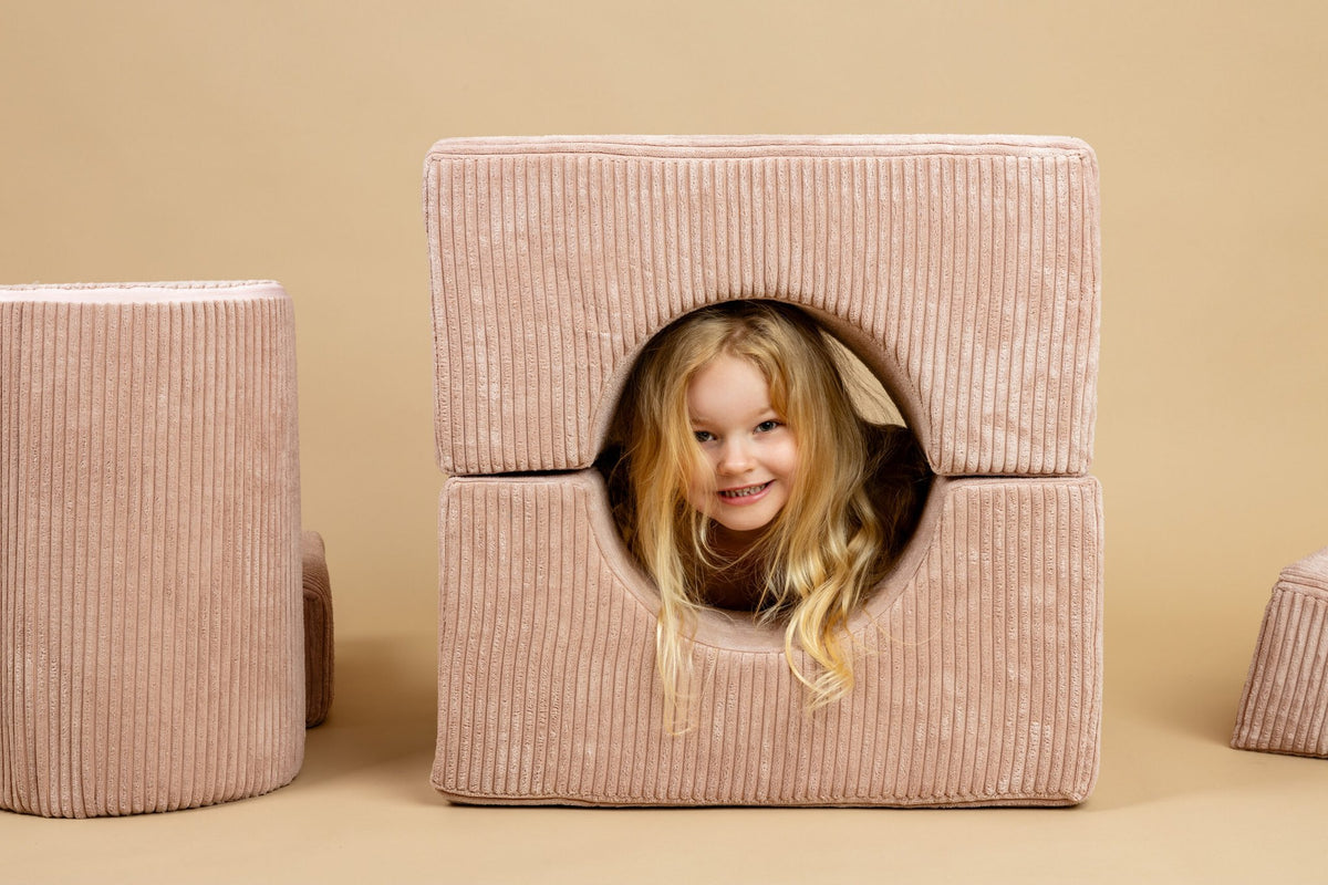 1. Young girl smiling through powder pink velvet corduroy shape set piece in playful setting