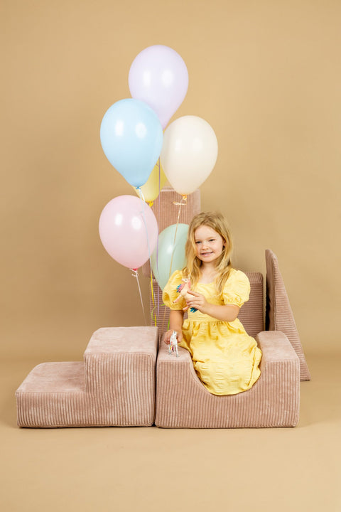 1. Young girl in yellow dress playing with powder pink shape set, holding colorful balloons in a playful indoor setting