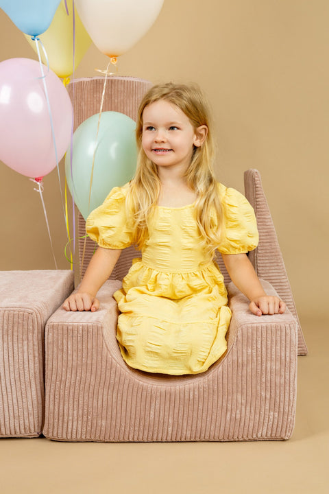 1. Girl in yellow dress sitting on powder pink shape set with pastel balloons in background