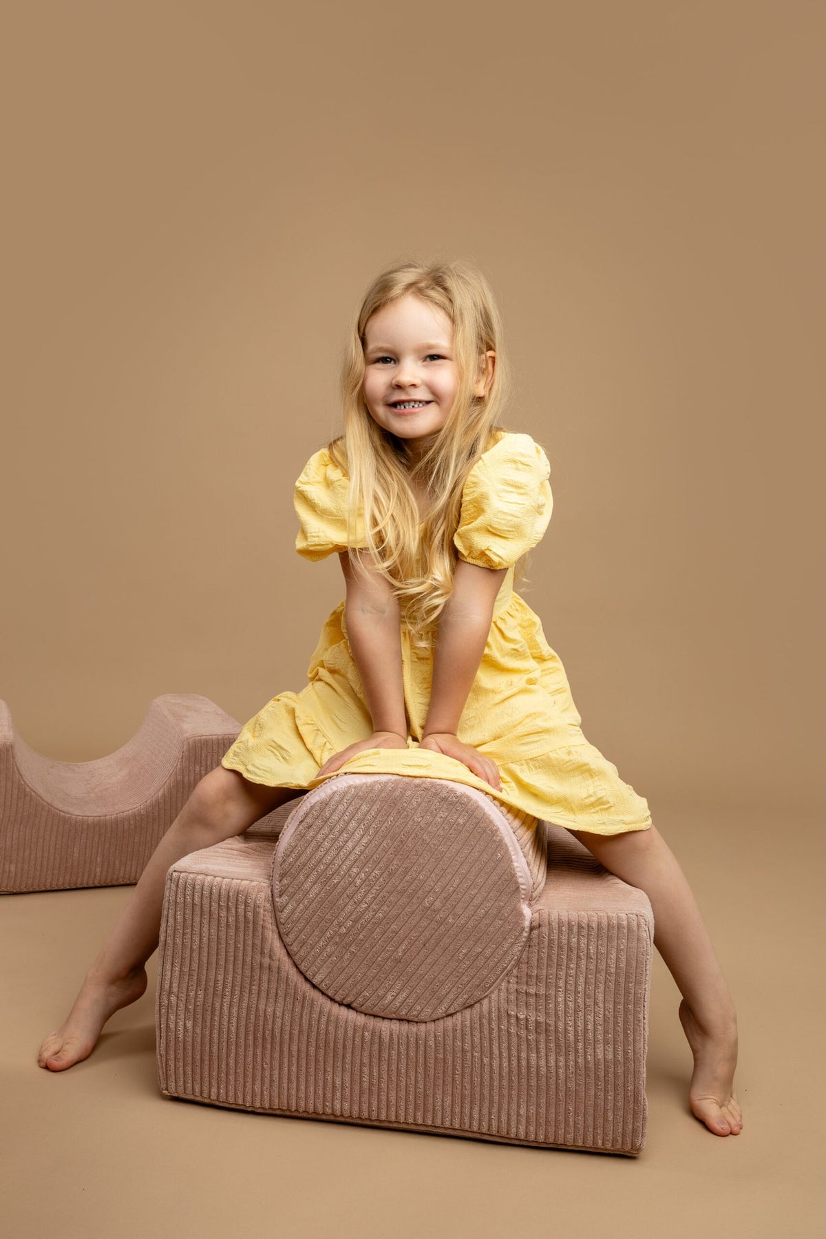 1. Girl in yellow dress sitting on powder pink velvet corduroy shape set in playful pose