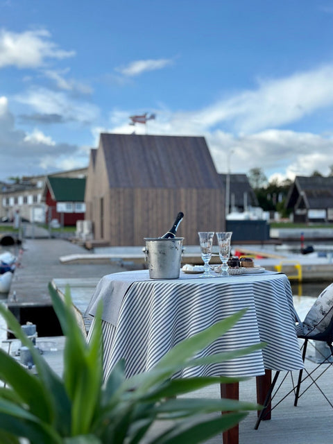 5. Scenic marina view with table set with Hortensias Home round tablecloth in beige with blue lines, featuring champagne and glasses