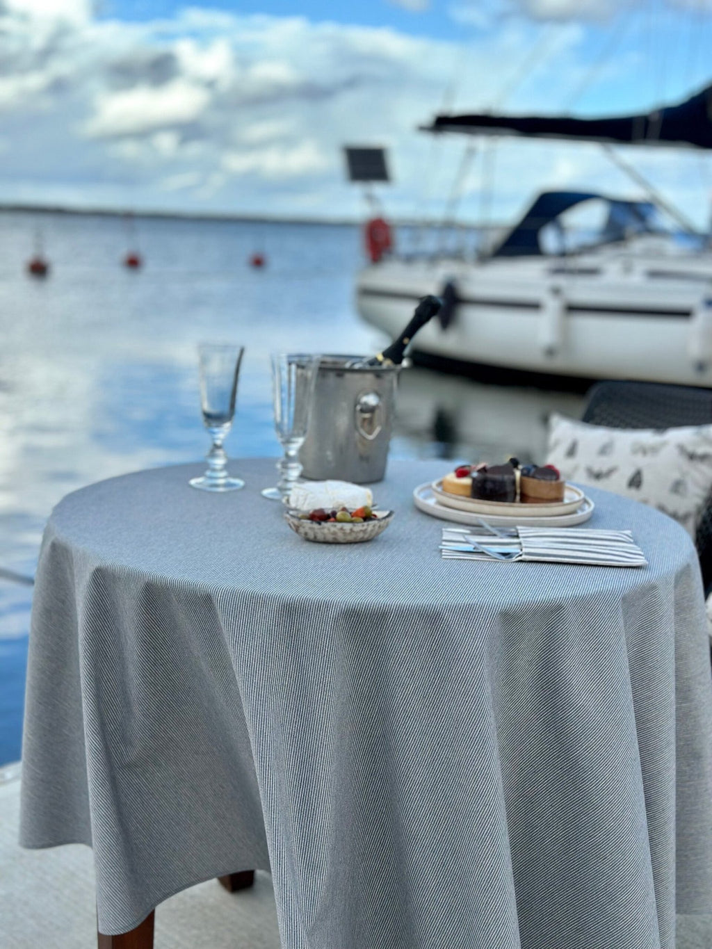 4. Outdoor setting with Nord 2 round tablecloth by Hortensias Home, featuring subtle blue lines on beige by the waterfront