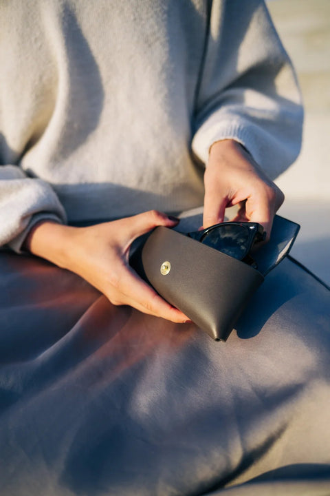 2. Woman placing sunglasses into Mirgoods black leather case, showcasing slim design, lifestyle setting