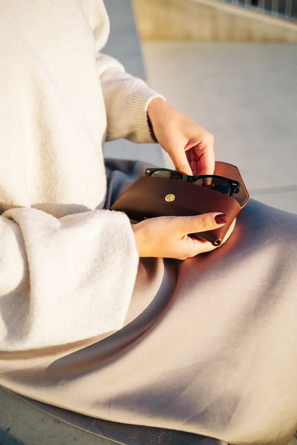 2. Close-up of Mirgoods dark brown leather sunglasses case in woman's hands, highlighting vegetable-tanned leather and soft lining