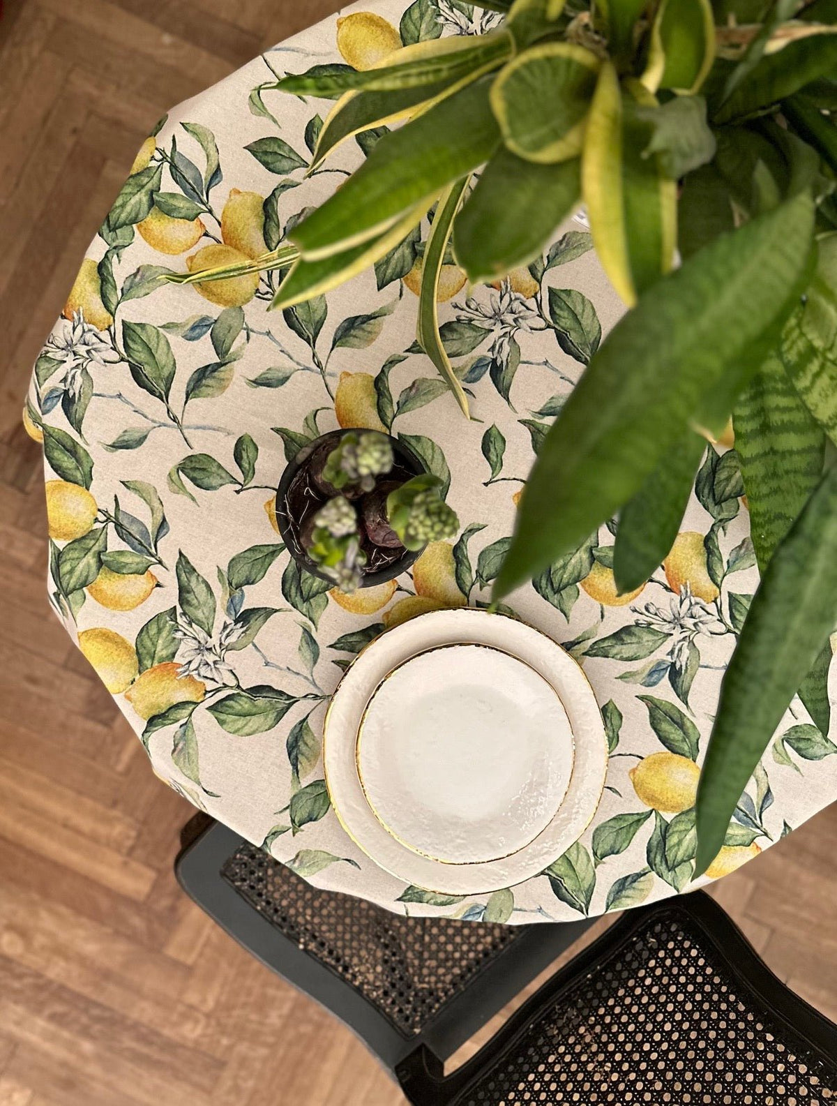 1. Top view of Hortensias Home Lemon Linen round tablecloth with vibrant lemon and leaf print, styled with plates and plant centerpiece