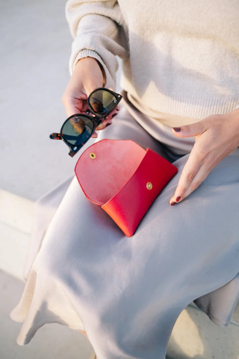2. Woman placing sunglasses into Mirgoods red leather case on her lap