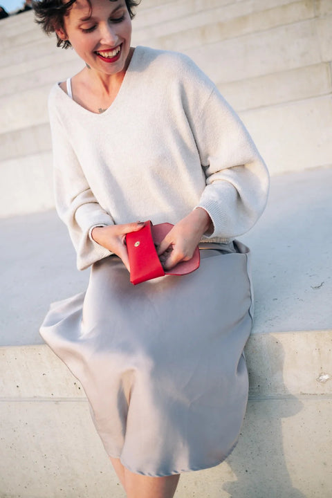 1. Woman holding Mirgoods red leather sunglasses case while sitting on steps