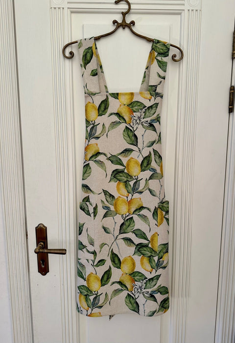 1. Women's lemon linen apron with crossed straps by Hortensias Home, featuring a vibrant lemon print, displayed hanging on a door