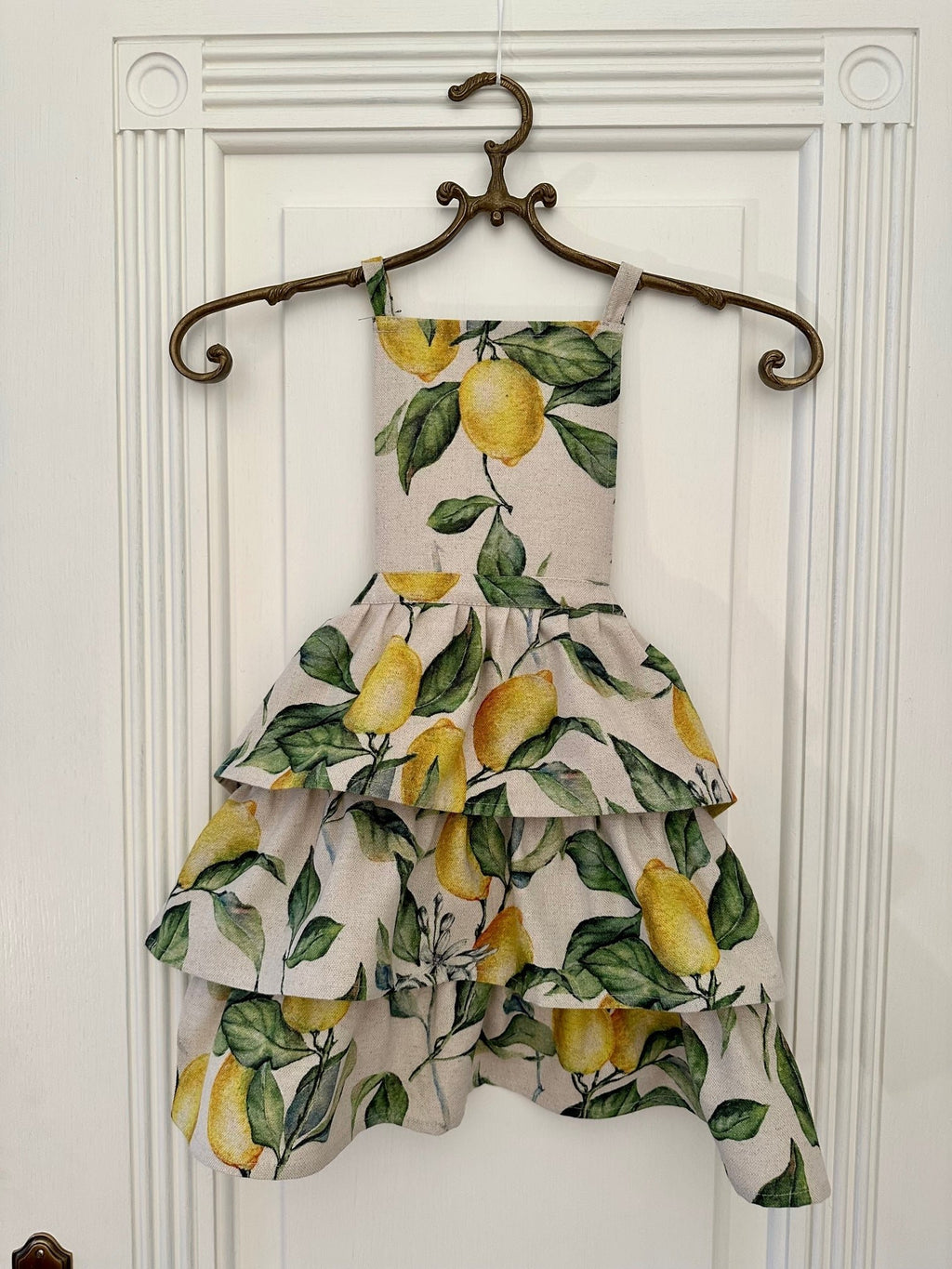 1. Kids apron with playful lemon print design by Hortensias Home, shown hanging on a decorative hanger