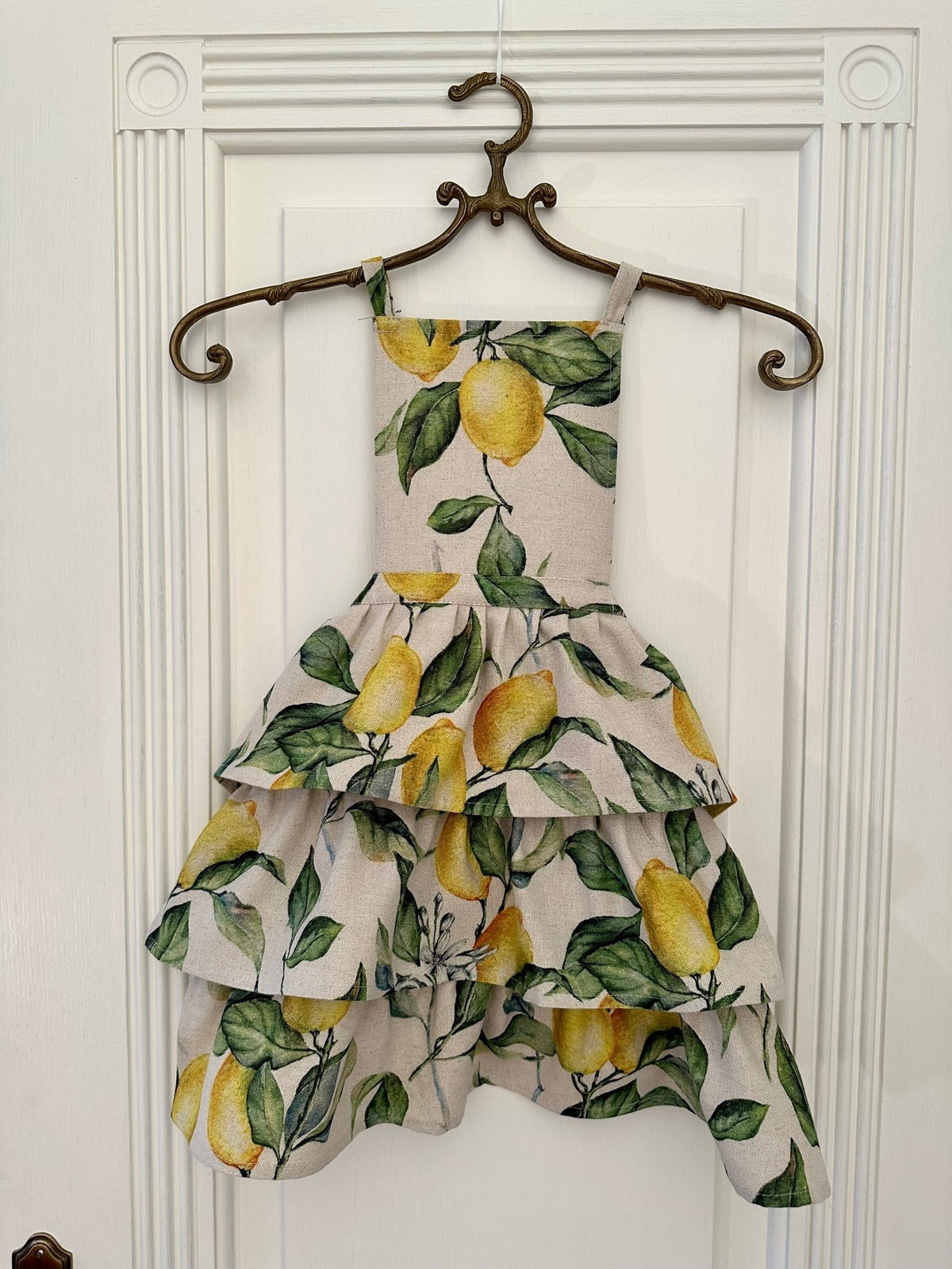 1. Kids apron with playful lemon print design by Hortensias Home, shown hanging on a decorative hanger