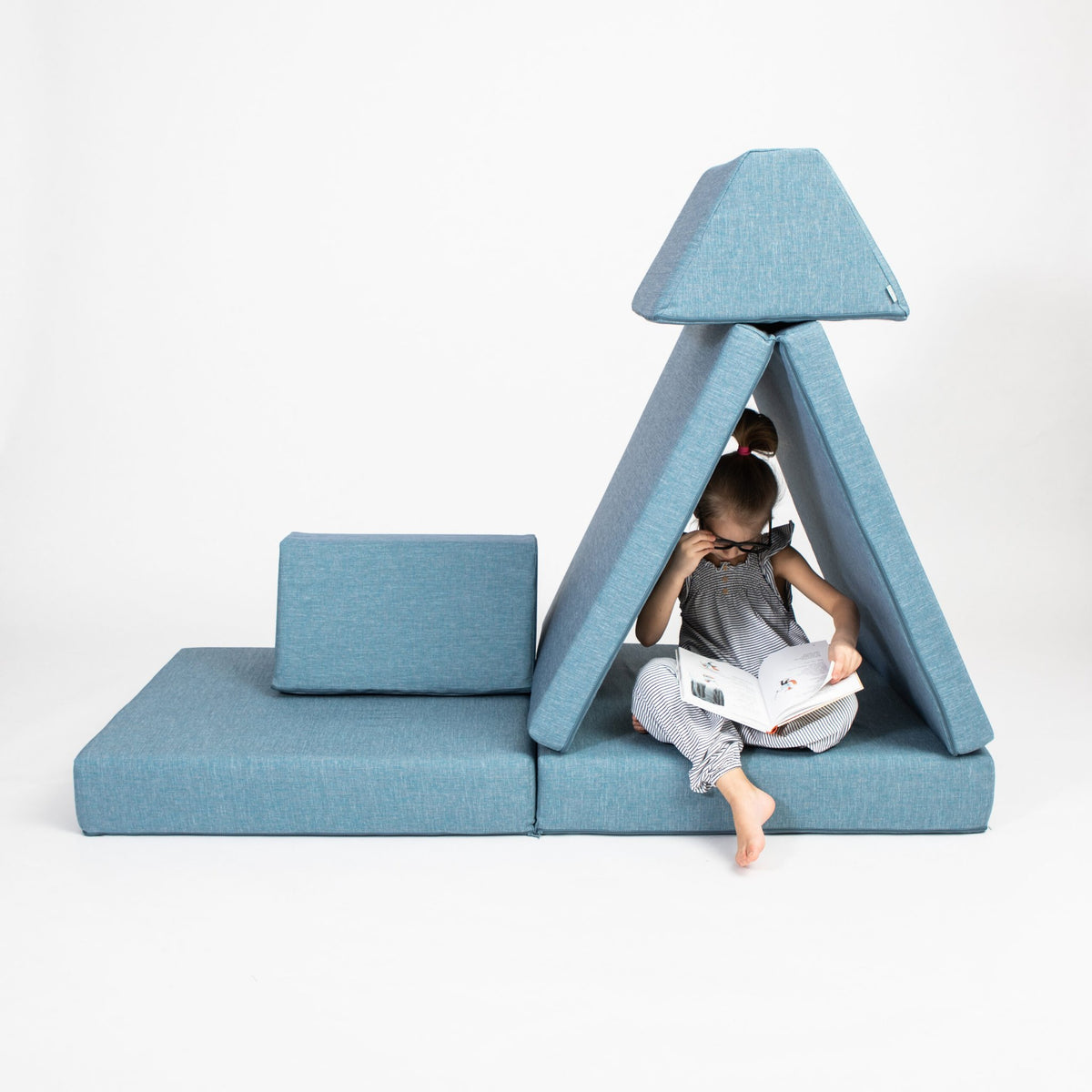 1. Child reading inside a turquoise play tent made from Monboxy activity play mattress set in a studio setting