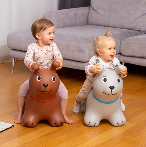1. Two toddlers playing indoors on brown and grey dog-shaped hopper toys