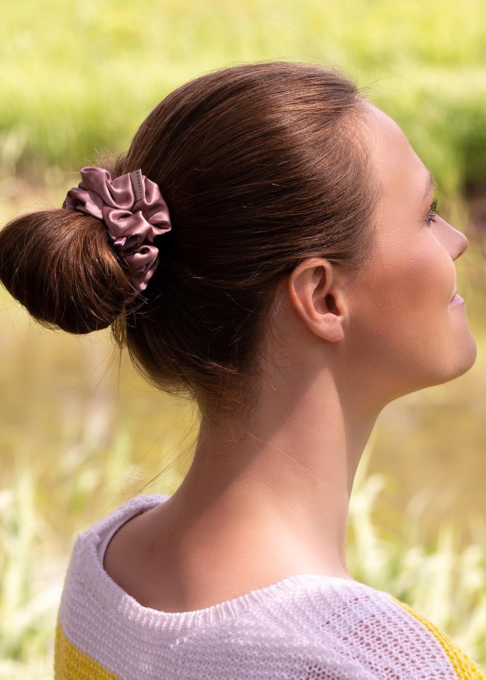1. Woman wearing Dondella luxury silk scrunchie in lilac, styled in a bun, outdoor setting