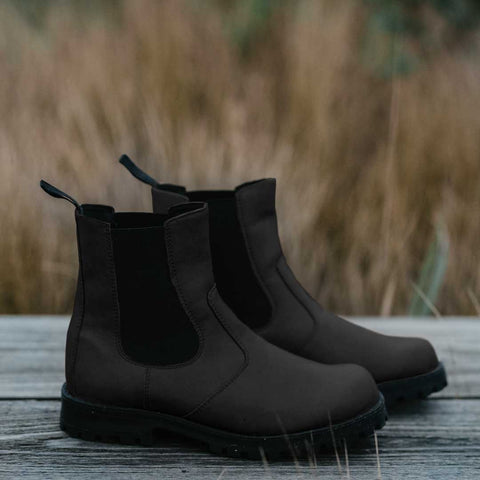 2. Pair of KIRA 3.0 Chelsea Boots in black on wooden surface with natural background