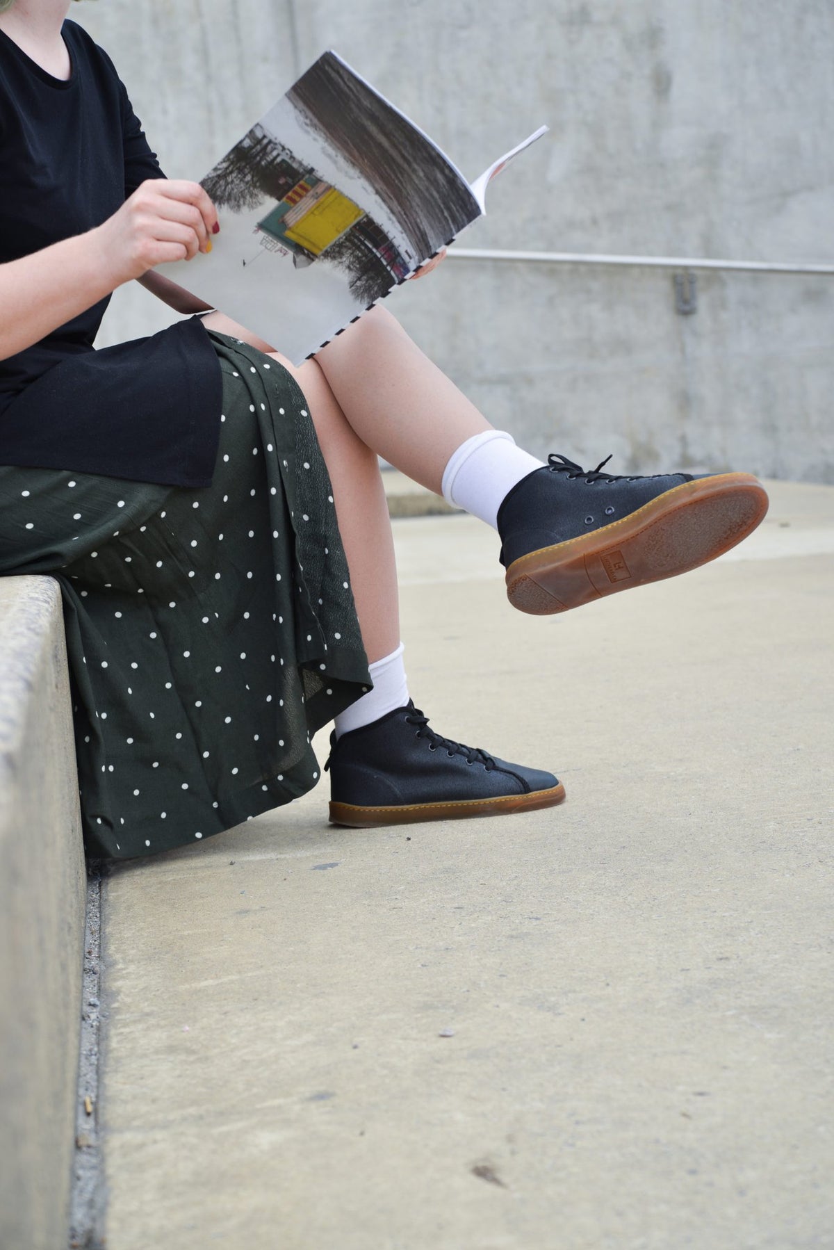 1. Unisex TOKU Stockholm Sneakers worn by a woman sitting on a concrete ledge, showcasing casual style