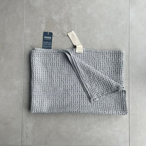 2. Folded gray waffle fabric towel with white hanger and KOOSdisain tag on concrete floor