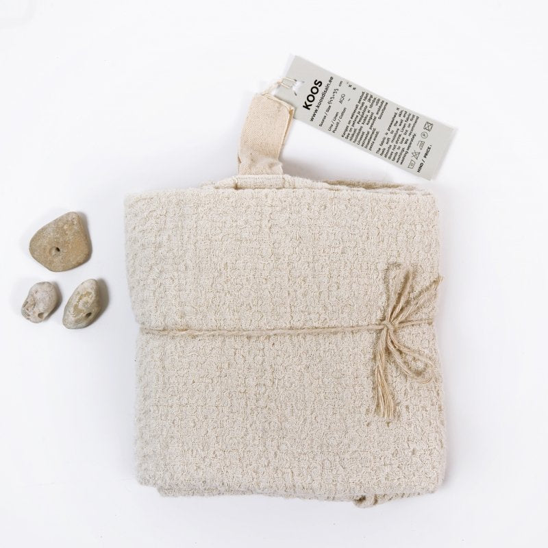 3. KOOSdisain big linen towel in textured white fabric folded with label and small stones