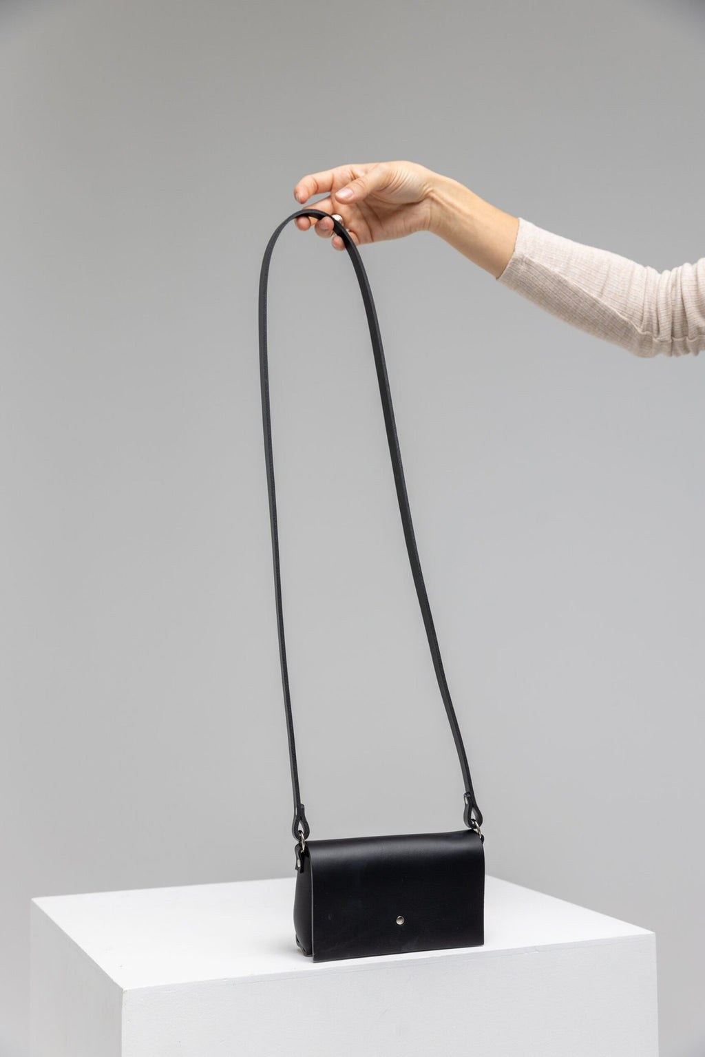 4. Hand holding PYKOK KORA minibag in black leather, showcasing long strap and minimalist design in studio