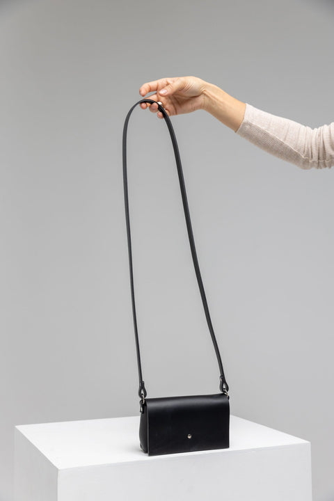 4. Hand holding PYKOK KORA minibag in black leather, showcasing long strap and minimalist design in studio