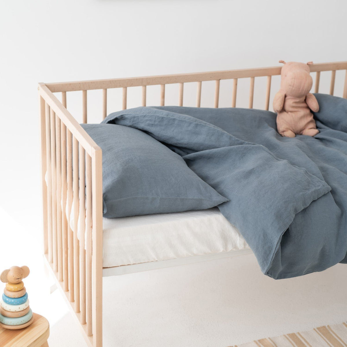 1. Blue fog linen duvet cover set on a crib with a plush toy, in a bright and airy nursery