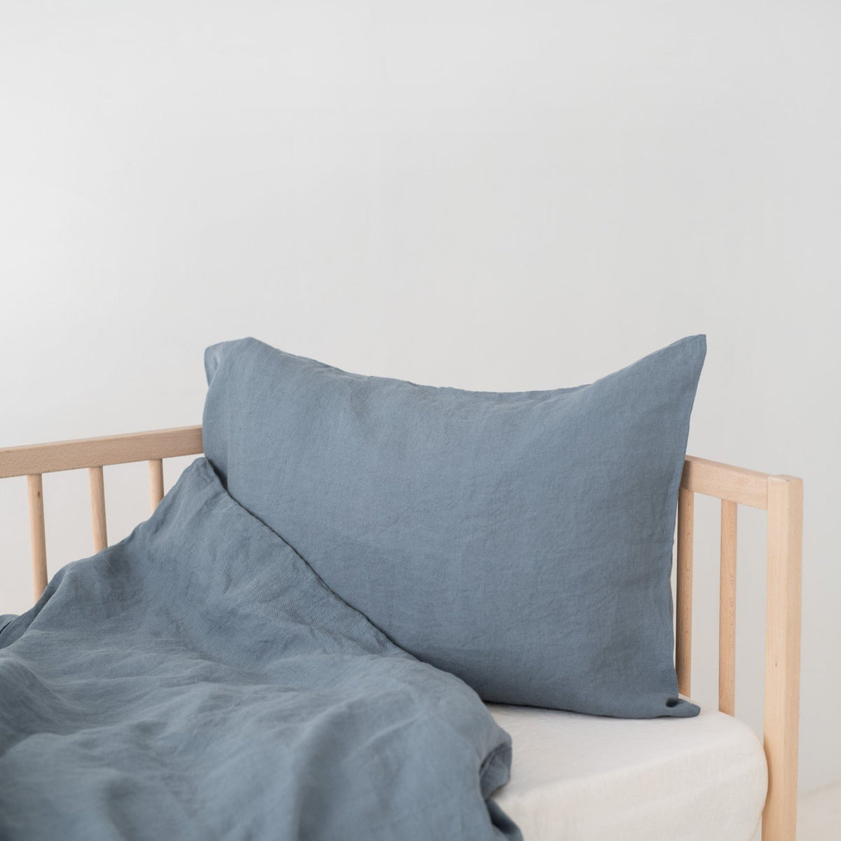 2. Blue fog linen pillow and duvet cover on a wooden crib, highlighting the soft and breathable fabric