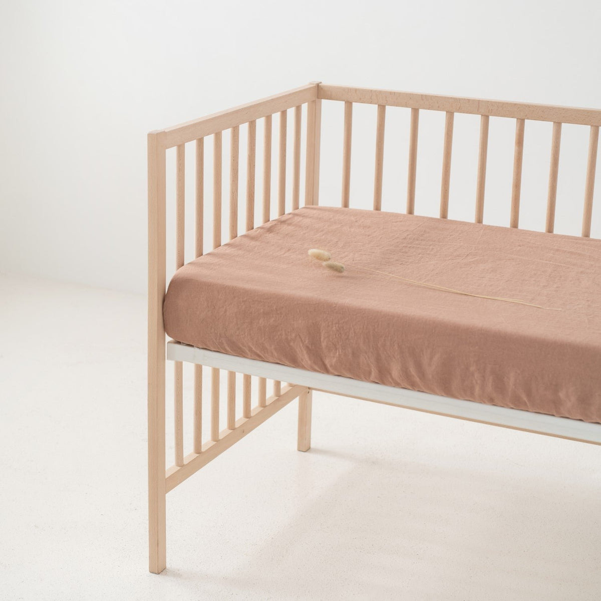 1. Cafe creme linen fitted sheet on a wooden crib in a minimalist room, showcasing the soft texture and elastic hem