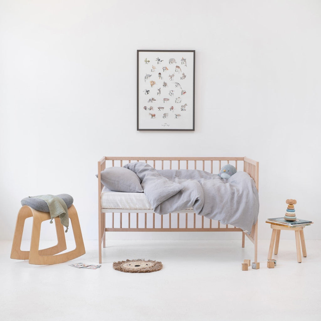 1. Light grey linen duvet cover set on a crib in a minimalist children's room with wooden furniture and decor