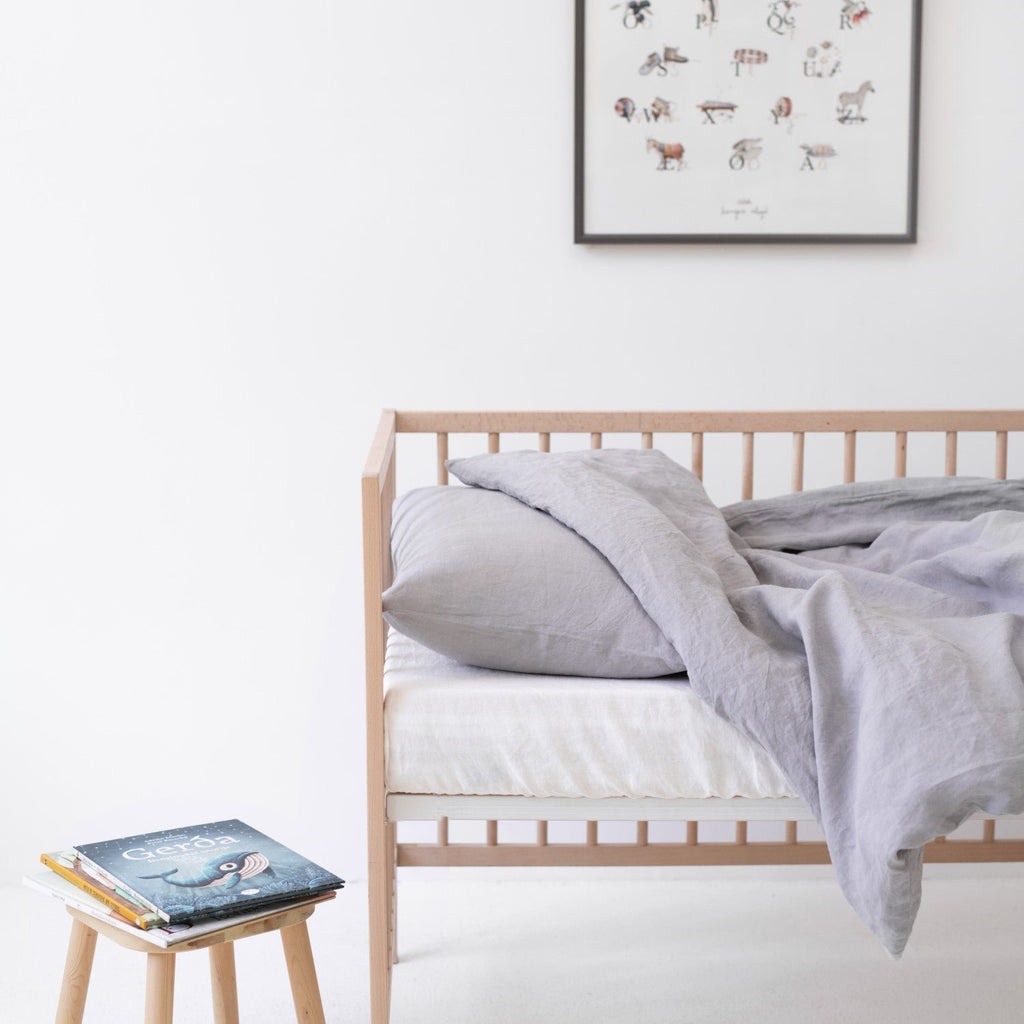 1. Light grey linen duvet cover set on a crib with a book on a stool, in a bright and airy children's room