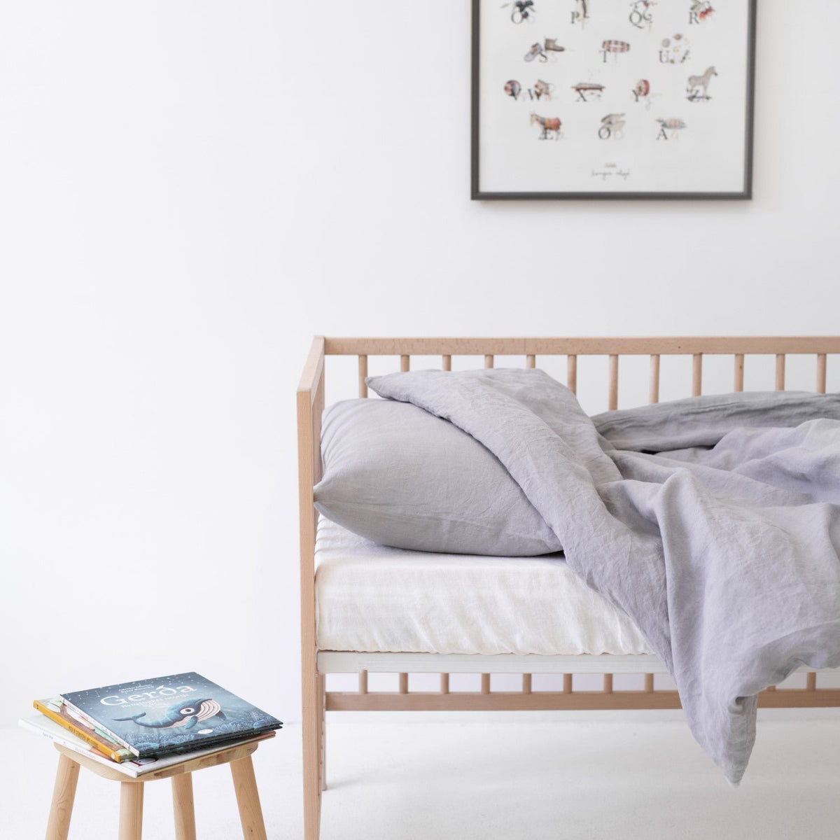 1. Light grey linen duvet cover set on a crib with a book on a stool, in a bright and airy children's room