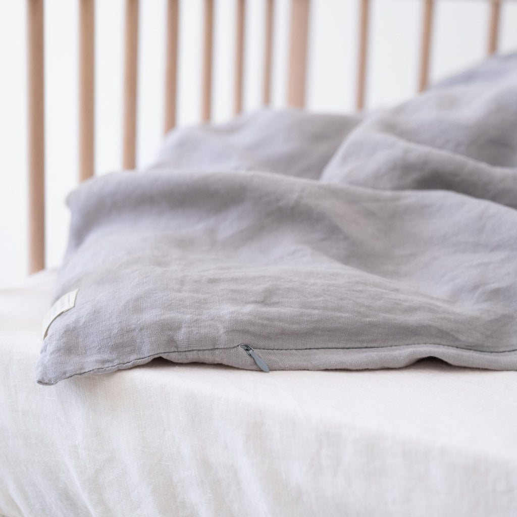 3. Close-up of light grey linen duvet cover edge on a crib, showing fabric texture and stitching detail