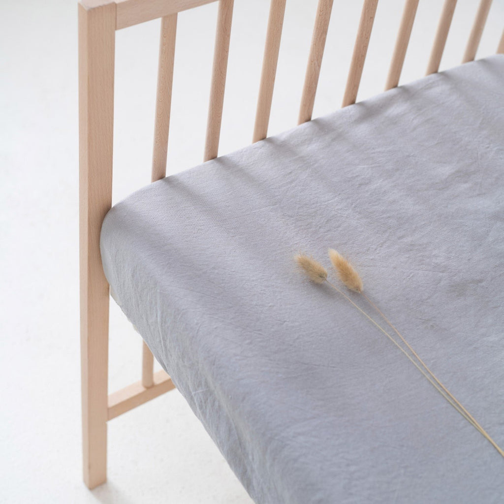 4. Close-up of light grey linen fitted sheet on a crib, showing fabric texture and elastic hem detail