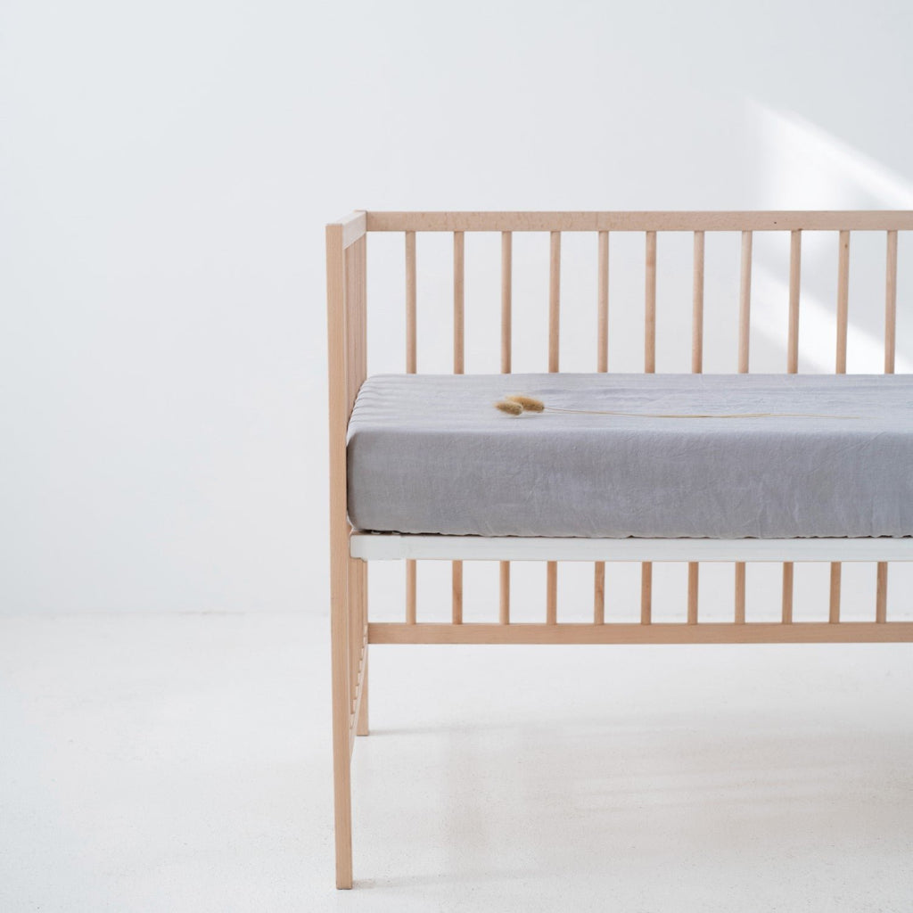 3. Light grey linen fitted sheet on a crib in a bright room, emphasizing the snug fit and soft material