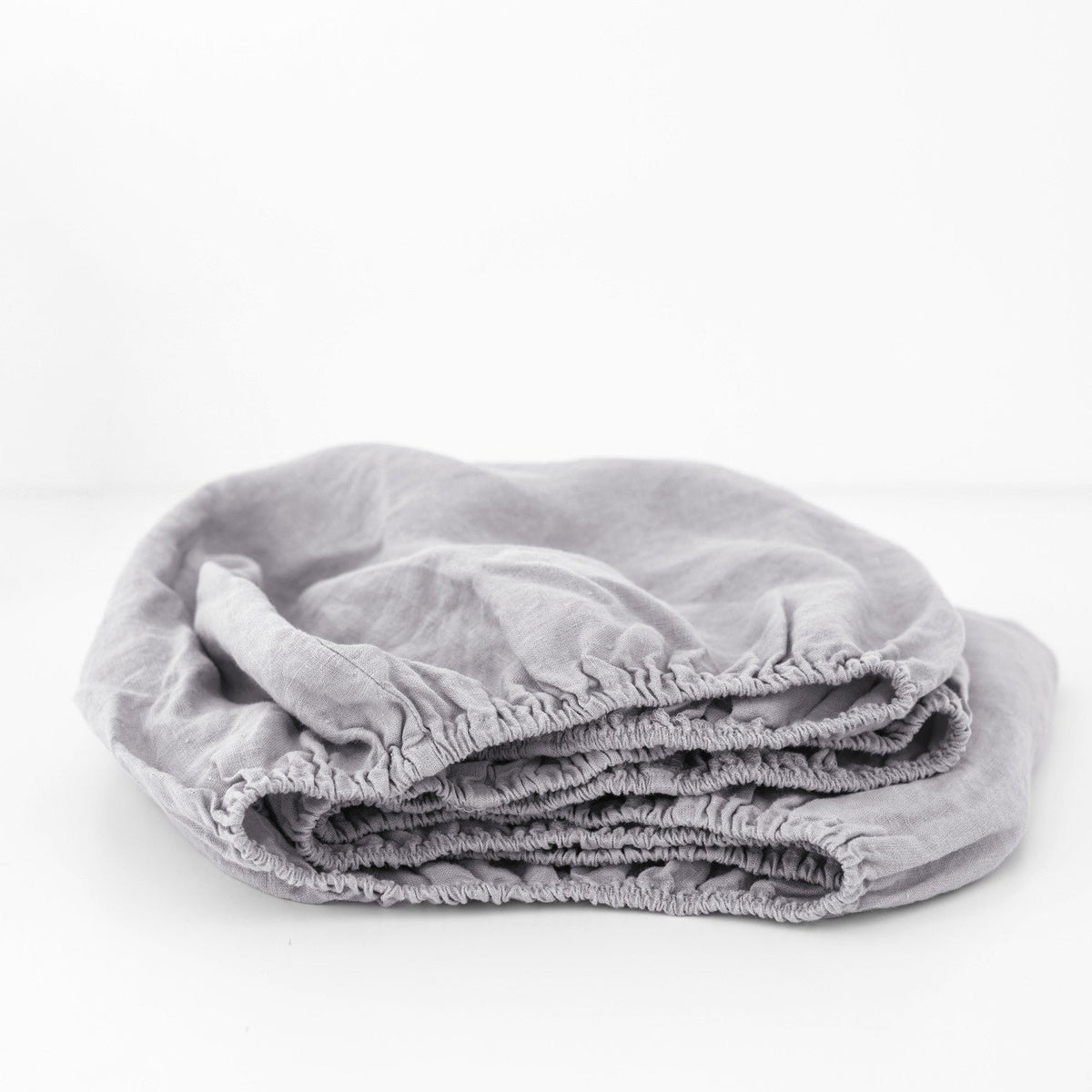 2. Folded light grey linen fitted sheet with elastic hem on a white background, highlighting fabric quality