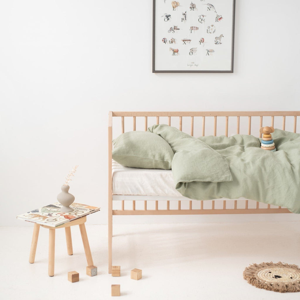 7. Side view of crib with sage green linen duvet cover set and wooden toys