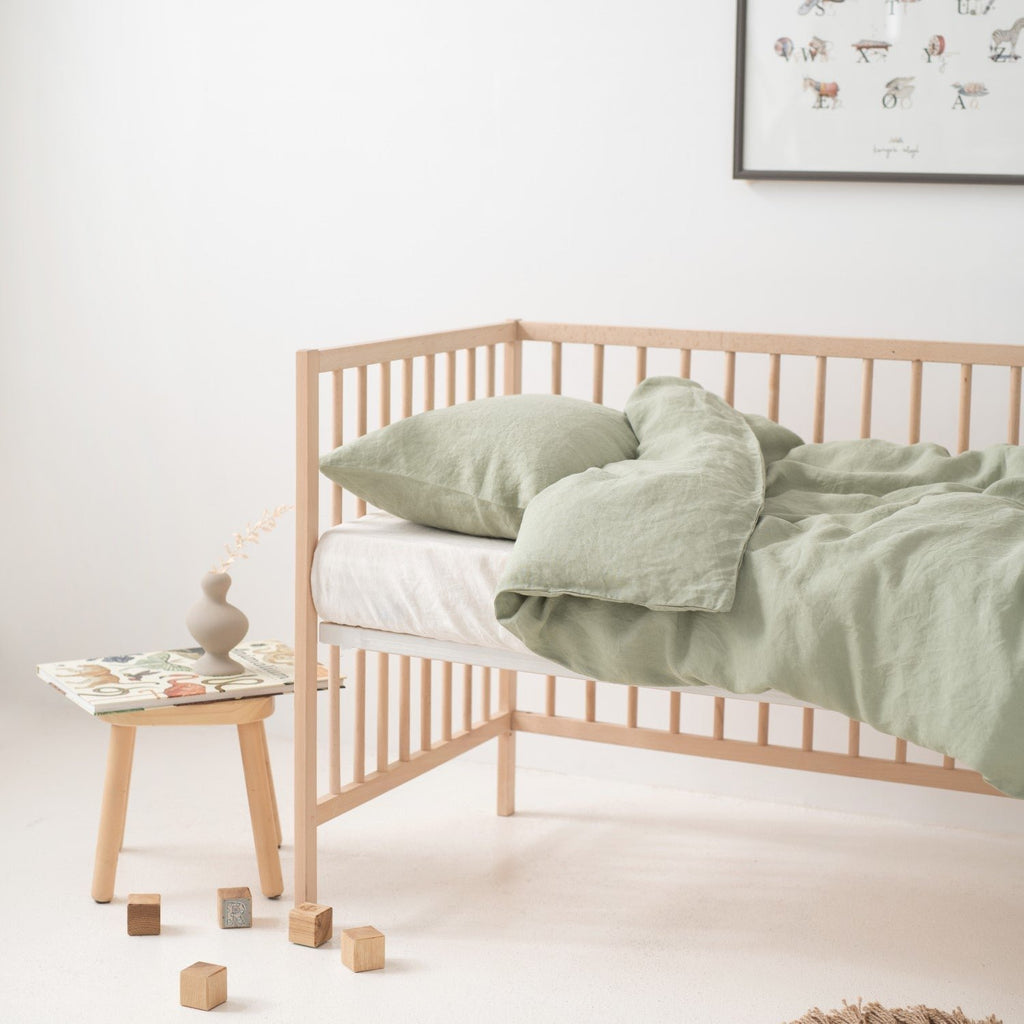 8. Crib with sage green linen duvet cover set, side table, and decor